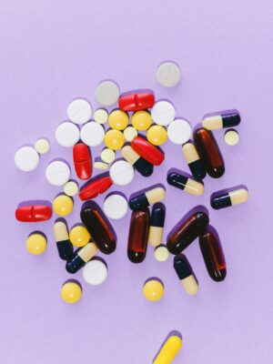 A collection of colorful capsules and tablets on a light purple surface.