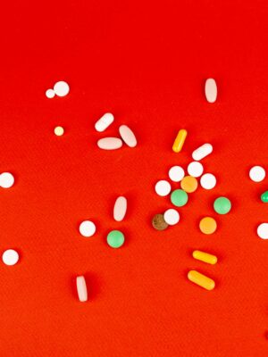 A variety of pills scattered on a vivid red surface, showcasing different shapes and colors.
